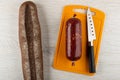 Loaf of bread, smoked sausage in polyethylene pack, knife on plastic cutting board on table. Top view Royalty Free Stock Photo