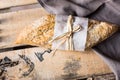 Loaf of rye whole wheat bread wrapped in parchment paper on linen napkin, plank wood background