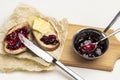 Loaf slices with butter and knife, jam on cutting board. Jam in a small metal bowl