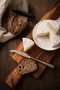 Loaf of soft blue cheese from cow milk on porcelain plate with walnut bread, knife, linen towel and dark brown wooden board as Royalty Free Stock Photo