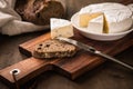 Loaf of soft blue cheese from cow milk on porcelain plate with walnut bread, knife, linen towel and dark brown wooden board as Royalty Free Stock Photo