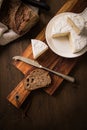 Loaf of soft blue cheese from cow milk on porcelain plate with walnut bread, knife, linen towel and dark brown wooden board as Royalty Free Stock Photo