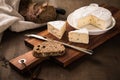 Loaf of soft blue cheese from cow milk on porcelain plate with walnut bread, knife, linen towel and dark brown wooden board as Royalty Free Stock Photo