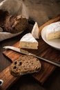 Loaf of soft blue cheese from cow milk on porcelain plate with walnut bread, knife, linen towel and dark brown wooden board as Royalty Free Stock Photo