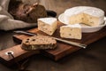 Loaf of soft blue cheese from cow milk on porcelain plate with walnut bread, knife, linen towel and dark brown wooden board as Royalty Free Stock Photo