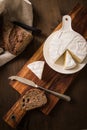 Loaf of soft blue cheese from cow milk on porcelain plate with walnut bread, knife, linen towel and dark brown wooden board as Royalty Free Stock Photo