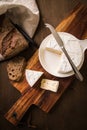 Loaf of soft blue cheese from cow milk on porcelain plate with walnut bread, knife, linen towel and dark brown wooden board as Royalty Free Stock Photo