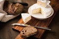 Loaf of soft blue cheese from cow milk on porcelain plate with walnut bread, knife, linen towel and dark brown wooden board as Royalty Free Stock Photo