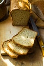 Loaf of sourdough bread cut into slices on wood cutting board, knife, kitchen table, sunlight flecks, cozy Royalty Free Stock Photo