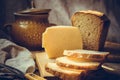 Loaf of sourdough sliced bread on wood cutting board, chunk of cheese, clay dishware, knife, rural kitchen interior Royalty Free Stock Photo