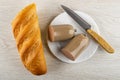 Loaf of bread, halves of liver sausage in polyethylene shell, knife in plate on wooden table. Top view Royalty Free Stock Photo