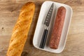 Loaf of bread, smoked sausage, knife in plate on wooden table. Top view Royalty Free Stock Photo