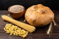 Loaf, wheat and pasta on dark wooden background