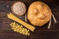 Loaf, wheat and pasta on dark wooden background