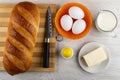 Loaf of bread, knife on cutting board, salt shaker, butter in saucer, eggs in bowl, jug of milk on table. Top view Royalty Free Stock Photo