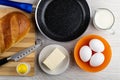 Loaf of bread, knife, salt on cutting board, frying pan, butter in saucer, eggs in bowl, jug of milk on table. Top view Royalty Free Stock Photo