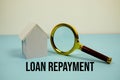 Loan Repayment text with White Model House and magnifying glass on blue background Royalty Free Stock Photo