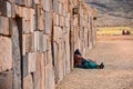 A local Andean lady rests against an intricately constructed stone wall at the Tiwanaku archaeological site, near La Paz, Bolivia
