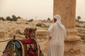 A local Arabic tour guide is standing by his dromedary camel by the ancient ruins of Palmyra