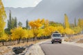 A local bus with luggage bags on the roof running along trees in autumn against mountain range.