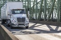 Local carrier white day cab big rig semi truck transporting cargo in dry van semi trailer driving on the arched truss bridge at Royalty Free Stock Photo