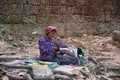 A local, elderly, cambodian woman is sitting on the roots of a giant spung tree and preparing colorful, traditional handcrafted