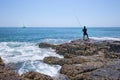 A local fisher man casting his fishing rod on rocks sea coast,the boat in the ocean, shore of the Bay in Asia, Thailand Royalty Free Stock Photo