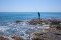 A local fisher man casting his fishing rod on rocks sea coast, shore of the Bay in Asia, Thailand Royalty Free Stock Photo