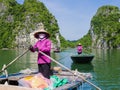 Local guides in typical purple uniforms and conical hats take tourists on a boat trip through the majestic limestone mountains of Royalty Free Stock Photo