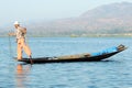 A local Intha fisherman holding a net and using one leg for rowing on a small wooden boat at Inle Lake in Myanmar