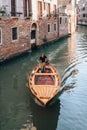 Local Italian man with a dog driving a small wooden boat on a narrow canal in Venice, Italy