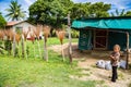 Local native indigenous Polynesian girl sells hand made brooms and plastic bags with sweet potato kumara, Tonga. A poor hut. Royalty Free Stock Photo