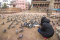 Local nepalese people world heritage ancient Patan Durbar Square, Kathmandu, Nepal.One woman sit on knee and feed pigeon on floor