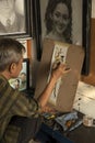 A local painter and cartoonist painting in his small studio and shop.