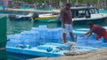 Local people of the Maldives stack water bottle packages on a small cargo boat.