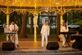 Local pop rock music band performs in gazebo of city public park, energetic outdoor performance