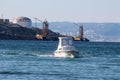 Local small white fishing boat coming in local harbour surrounded with blue sea and industrial complex in background Royalty Free Stock Photo