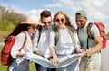 Local travel. Group of young people studying map on roadside, checking their destination point, hitchhiking for car Royalty Free Stock Photo