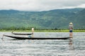 Local young Burmese fisherman wearing a checked shirt rowing after fishing, standing on boat's stern