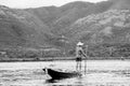 Local young Burmese fisherman wearing a checked shirt rowing after fishing, standing on boat's stern