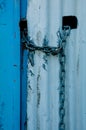 Lock and chain on a white corrugated iron wall with a blue door Royalty Free Stock Photo