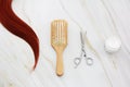 A lock of red female hair, a comb, scissors and a care cream Royalty Free Stock Photo