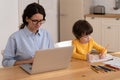 Lockdown, family, distance job. Child painting while his mother working on laptop at home office. Royalty Free Stock Photo