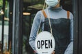 Lockdown. waitress staff woman wearing protection face mask turning OPEN sign board on glass door in modern cafe Royalty Free Stock Photo