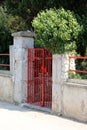 Locked front yard red metal entrance doors mounted on dilapidated stone and concrete fence pole surrounded with paved road