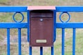 Locked old dilapidated metal mailbox mounted on strong blue iron fence in family house driveway