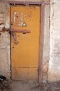 Locked old rusty yellow door with high voltage sign. Grey wall of transformer substation, closed padlock Royalty Free Stock Photo