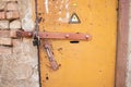 Locked old rusty yellow door with high voltage sign. Grey wall of transformer substation, closed padlock Royalty Free Stock Photo