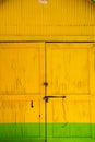 Closed yellow door of wooden barn with green stripe as background