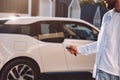 Locking the vehicle. Young stylish man is with electric car at daytime